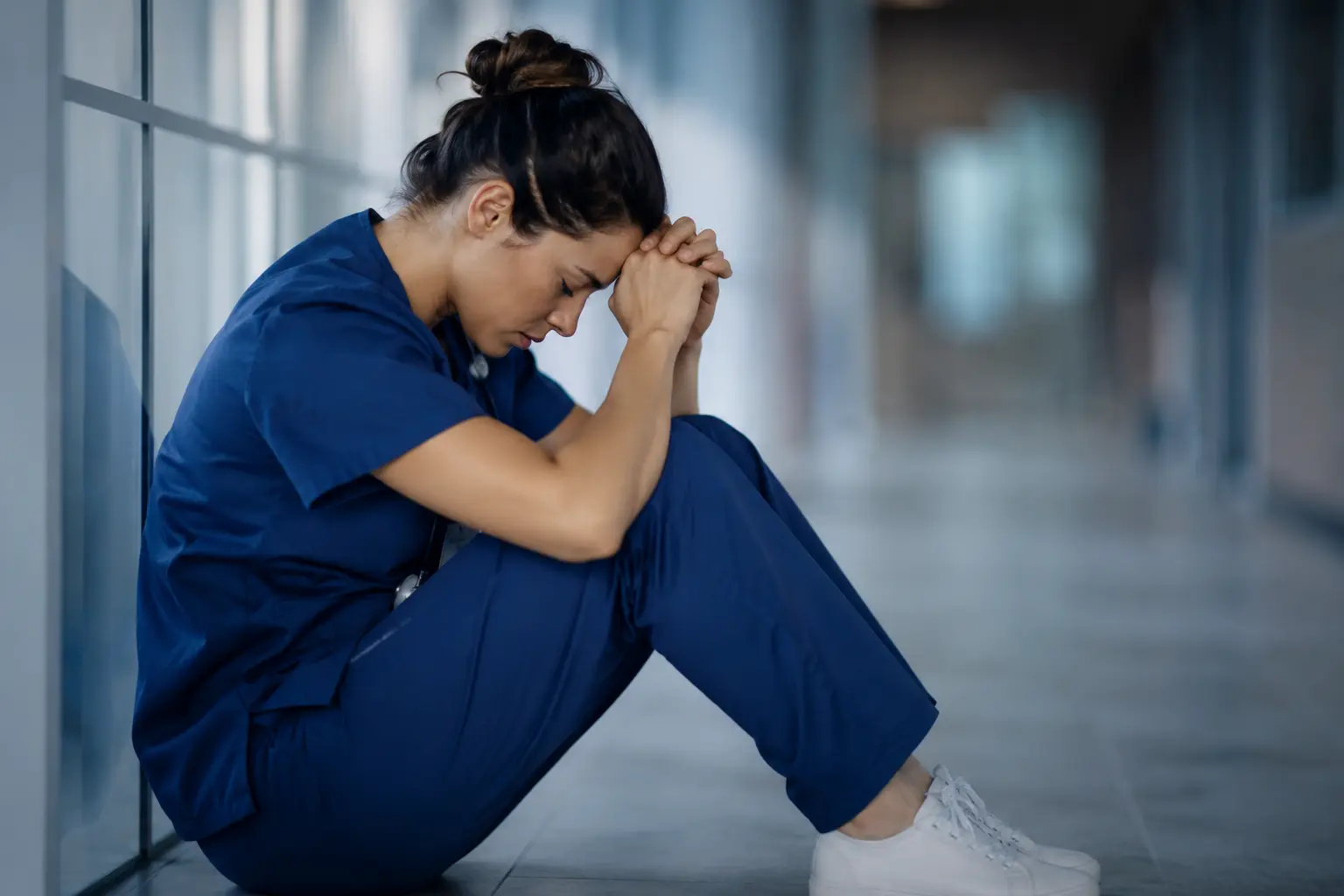 Healthcare professional sitting alone in a hospital corridor looking emotionally exhausted and overwhelmed, illustrating compassion fatigue in helping professions and the emotional impact of caregiving roles 